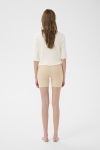 Bézs színű, rugalmas rövidnadrág sima textúrával, fehér, enyhén texturált inggel párosítva, amelyen csipkés ujjvég található.