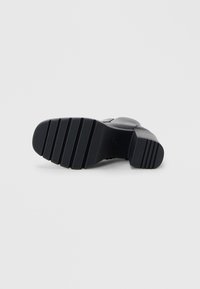 Stivale nero alla caviglia con suola in gomma testurizzata, caratterizzato da un tacco spesso e modelli scanalati per una migliore presa. Parte superiore in pelle liscia con dettagli minimi.