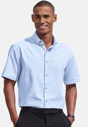 Hellblaues kurzärmeliges Hemd mit knopflosem Kragen und strukturiertem Finish, aus Kunststoff gefertigten Knöpfen. Kombiniert mit schwarzen Hosen und einem Gürtel.