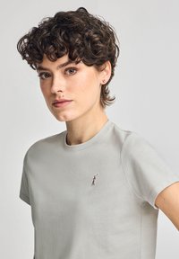 T-shirt in cotone grigio chiaro con maniche corte, caratterizzata da un piccolo design ricamato di una figura che tiene un bastone da golf sul petto.