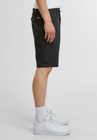 Pantaloni cargo neri realizzati in tessuto resistente, caratterizzati da molteplici tasche, una vestibilità comoda e un discreto logo sul retro. Indossati con sneaker bianche.