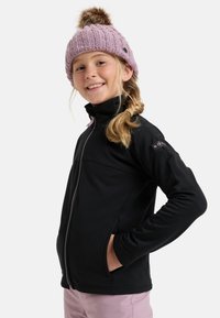 Černá zapínací bunda se stojáčkem a dvěma bočními kapsami. Na hlavě má růžovou pletenou čepici s bambulí nahoře.