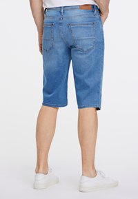 Dżinsowe szorty w jasnoniebieskim kolorze, o długości do połowy uda, z tylnymi kieszeniami i delikatnym wyblaknięciem. W zestawieniu z białymi sneakersami dla casualowego wyglądu.