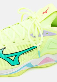 Zapatilla deportiva amarillo neón con parte superior texturizada, acentos en negro y turquesa, y suela multicolor que presenta detalles en rosa y azul.