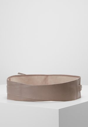 Large ceinture en cuir taupe avec un design enveloppant, présentée à plat sur une surface blanche sur un fond uni.