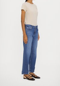 Beige katoenen t-shirt, blauwe rechte jeans met vijf zakken en zwarte ballerina's met banden en decoratieve hardware.