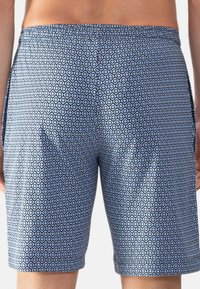Close-up van een persoon die blauwe zwembroeken draagt met een klein zwart-wit geometrisch patroon, gezien vanuit de rug.