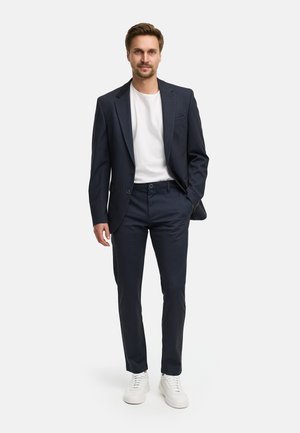 Traje azul marino con blazer de un solo pecho, pantalones a juego y camiseta blanca. Combinado con zapatillas blancas para un look casual.
