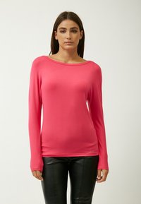 Langärmliges pinkes Oberteil aus weichem Stoff, mit weitem Ausschnitt und taillierter Form, kombiniert mit schwarzen Lederhosen.