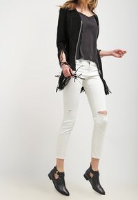 Black suede jacket with fringe details, paired with a black top, white distressed jeans, and black ankle boots featuring gold accents.