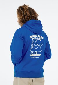 Blauwe hoodie van een katoenmix met een afbeelding van een lachende berg met een skistok en de tekst "SNEAK PEAK" in het wit op de achterkant.