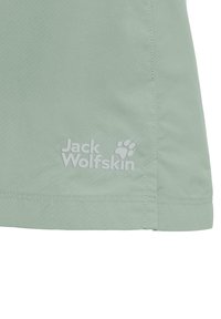 Tissu vert clair avec des coutures doubles et un logo blanc Jack Wolfskin comportant une empreinte de patte près du bord inférieur.