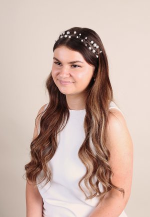 Perlenakzentiertes Haarband mit silbernem Draht, verziert mit kleinen runden Perlen, getragen von einer Person mit langen, welligen braunen Haaren, vor einem hellen Hintergrund.
