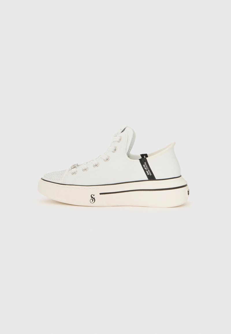 Sneaker bianca a basse top con suola spessa, rifiniture nere, occhielli argentati e etichetta "Skechers Slip-Ins" sul lato.