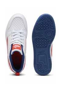 Baskets blanches avec des accents rouges et bleus, détails perforés, semelles en caoutchouc plates et logo de marque bien visible sur la languette et sur le côté.