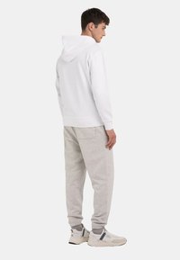 Hvid hættejakke parret med lysegrå joggere. Outfittet bliver afsluttet med chunky hvide sneakers med sorte accenter.