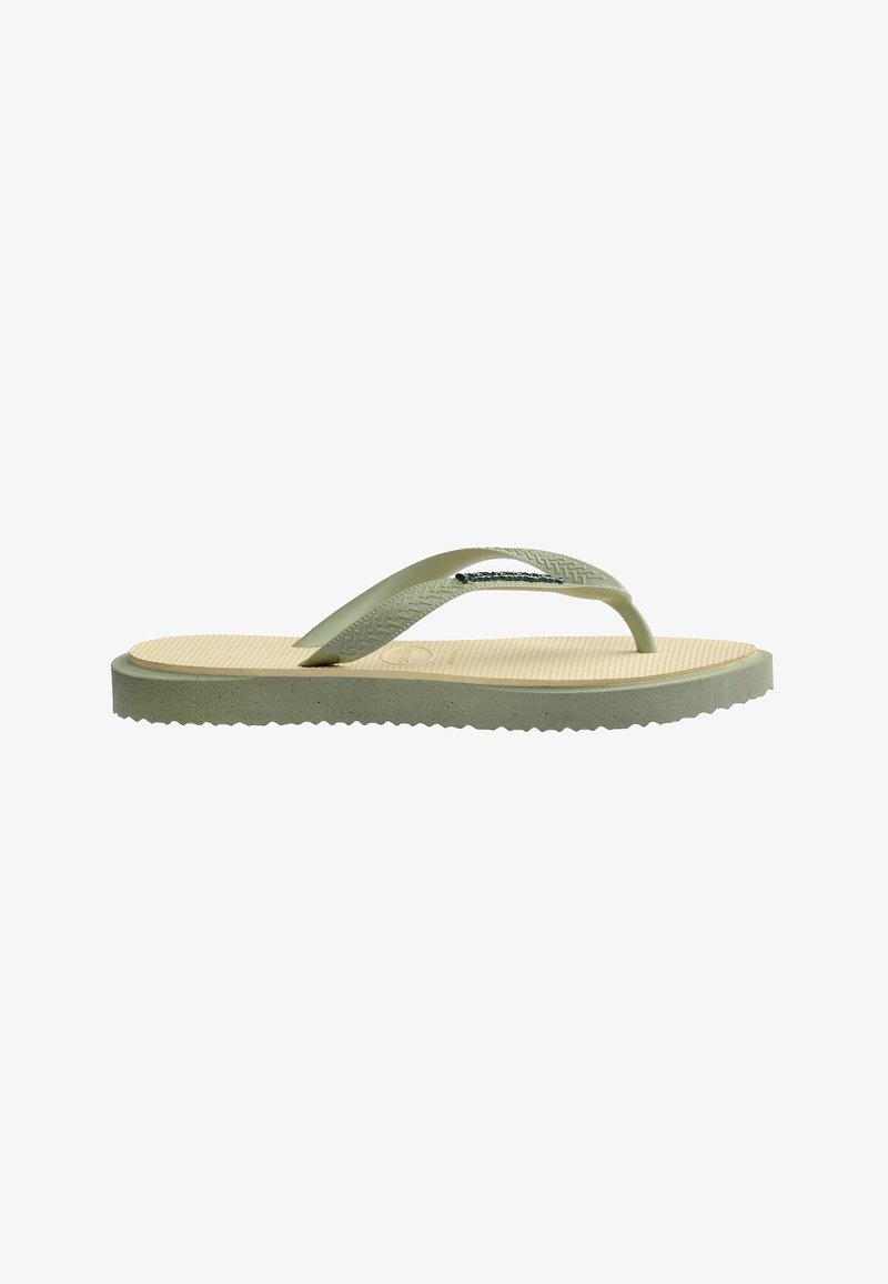 Une sandale flip-flop beige avec une semelle texturée et des sangles vert olive à motifs, présentée sur un fond blanc.