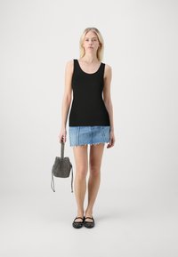 Svart linne, denim minikjol och svarta lägenheter. Modellen håller en liten mönstrad bucket bag. Enkelt, avslappnat outfit.