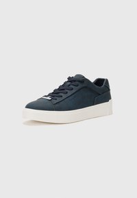 Tênis de couro azul-marinho com bico arredondado, sola branca e atacadores planos. Apresenta o logótipo da marca em relevo na lateral e uma textura suave.