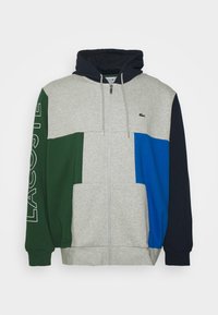 Felpa con cappuccio con zip a blocchi di colore in grigio, verde, blu e blu navy. Presenta un cappuccio con coulisse, tasche a marsupio e logo ricamato sul petto.