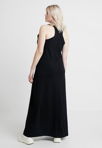 Fekete maxi ruha ujjatlan kivitelben, puha anyagból, testhezálló felső résszel és bővülő szoknyával. Fehér sportcipővel viselve a laza stílusért.