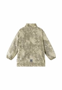 Veste imperméable légère beige avec un motif de fougères, col montant, poignets élastiques, et un écusson gris avec logo sur le bas du dos.