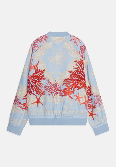 Šviesiai mėlyna bombonešio striukė su sudėtingais raudonais koralų ir smėlio spalvos jūros motyvais. Raukšlėti rankogaliai ir apatinė dalis, su laisvu siluetu ir siuvinėtais detalėmis.