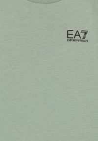 Svetlozeleni kratkoročni T-majica iz mehkega materiala, s črnim logotipom "EA7 Emporio Armani" na levi strani blizu vratu.