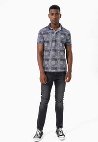 Kortærmet polo shirt i nuancer af blå og grå med ternet mønster, parret med mørke slidte jeans og sorte sneakers.