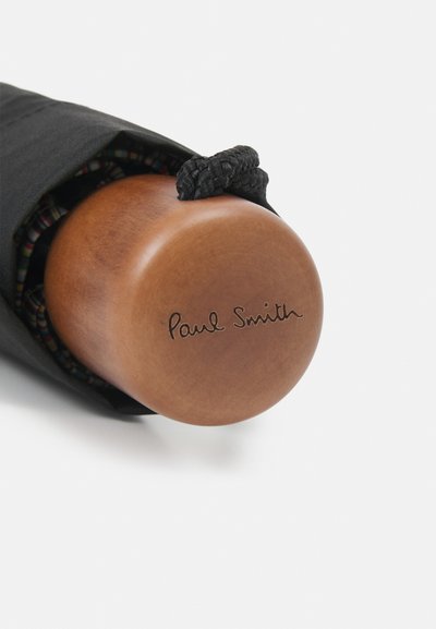 Crni platneni zaštitni omotač za kišobran s zaobljenom drvenom drškom na kojoj je ugraviran potpis "Paul Smith". Uključena je podešavajuća crna pletena traka.