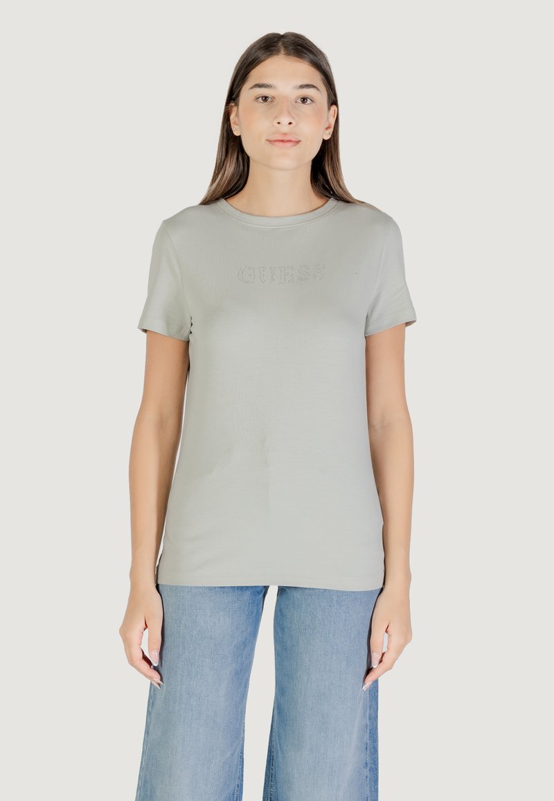T-shirt verde chiaro a maniche corte realizzato in tessuto morbido, con logo 'GUESS' in rilievo sul petto. Abbinato a jeans blu a gamba larga.