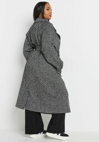 Trencz w wzór houndstooth w czerni i bieli z paskiem w talii, z szerokim kołnierzem i długim krojem, zestawiony z szerokimi spodniami.