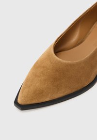 Καφέ σουέντ επίπεδο παπούτσι με μύτη σε σχήμα αιχμής και μαύρη ελαστική σόλα. Λείο εσωτερικό με σχεδιασμό χαμηλής κοπής γύρω από τον αστράγαλο.