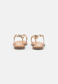 Sandalias planas marrón con tiras metálicas doradas, con un diseño sencillo y una textura suave. Suela delgada con acentos de hardware mínimos.