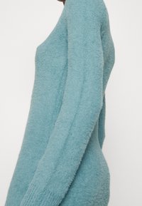 Ljusblå tröja, mjuk textur, lös passform, långa ärmar, ribbade detaljer vid manschetterna och en vid kragsdesign.