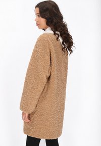 Cappotto beige, oversize, morbido, realizzato in tessuto testurizzato, con una vestibilità ampia e maniche lunghe, che arriva a metà coscia.