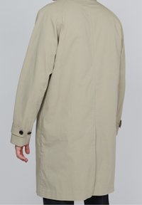 Beige ytterrock med rak skärning, knäppta manschetter och en slät yta. Har en söm bak och en minimalistisk design.