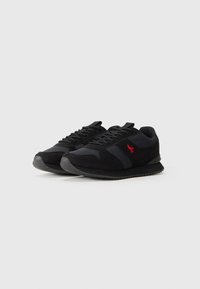 Pair of black low-top sneakers with dark gray panels, black laces, and a small red embroidered bird logo on the side.