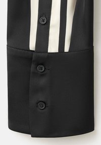 Manșetă de cămașă neagră cu două nasturi negri și un model vertical în dungi alb-negru deasupra manșetei.