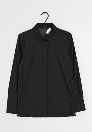 Černá košile s dlouhým rukávem a knoflíky, s límečkem, zavěšená na černém ramínku na bílém pozadí.