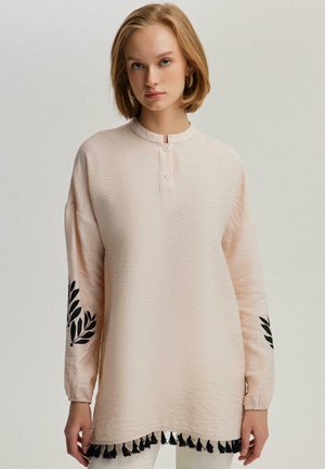 Lichtroze langemouwen top met een mandarin collar, knoopsluiting, zwarte bladen borduursel op de mouwen en een franjesrand. Gestructureerde stof.