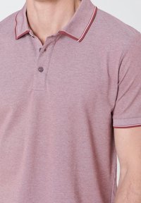 Polo à manches courtes en mauve avec un tissu texturé, col et bords de manches rayés contrastants, doté d'une patte à deux boutons.