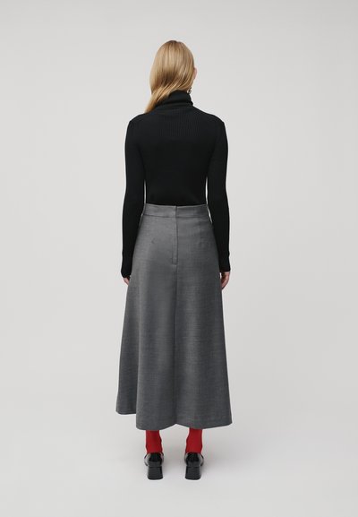 Maglione a collo alto nero a coste, gonna grigia a tutta lunghezza con texture liscia, collant rossi e scarpe nere in pelle verniciata. Vista da dietro.