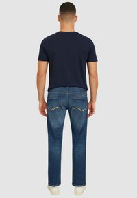 Casual outfit voor heren met een marineblauwe t-shirt en blauwe jeans met een rechte pasvorm. De jeans hebben opvallende stiksels op de achterzakken.