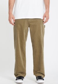 Pantalons en velours côtelé vert olive à coupe ample, dotés de poches latérales et d'une texture douce. Associés à des baskets noires.