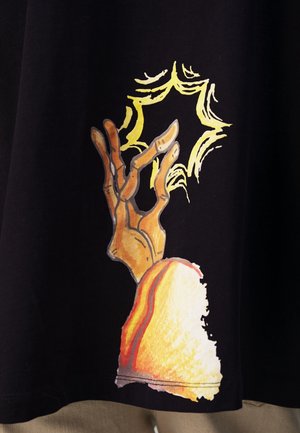 Hand met vingers die een gloeiende, gele stervorm vasthouden, met een mouw in oranje- en gele tinten op een zwarte achtergrond.