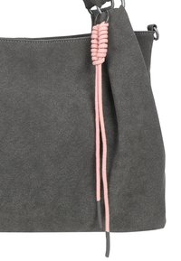 Borsa in suède grigio scuro con manico spesso e cordoncino decorativo rosa chiaro avvolto attorno a un anello di metallo vicino al manico.