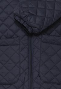 Tamnoplava prošivena jakna s patentnim zatvaračem, s elastičnim manšetama i dva prednja džepa. Glatki, lagani materijal sa suptilnim sjajem.