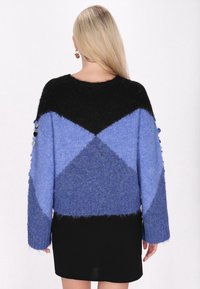 Maglione in maglia oversize con un motivo geometrico nero e blu; presenta maniche lunghe e tessuto texturizzato. Gonna nera sotto.