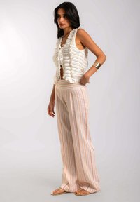 Top blanco de punto sin mangas con bordes volados y diseño calado, combinado con pantalones de pierna ancha con rayas claras en colores pastel.